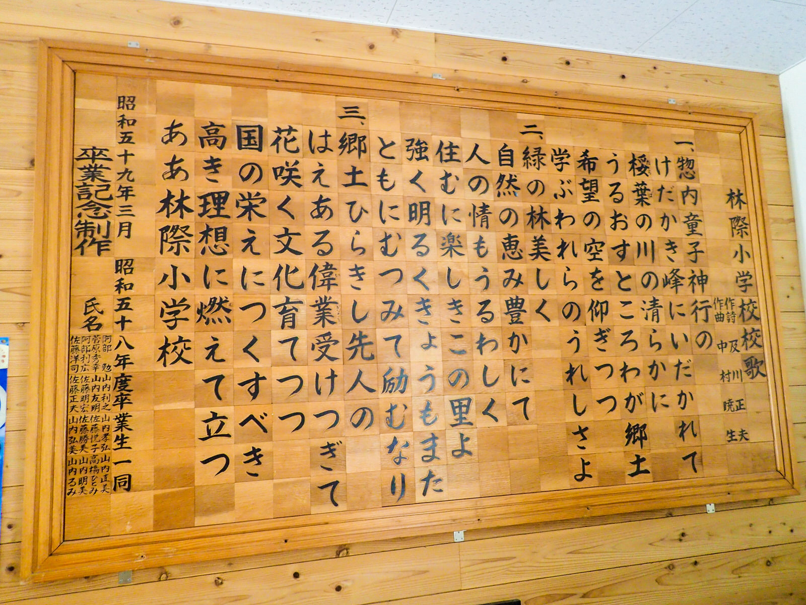 卒業記念として制作された木の板に書かれた林際小学校の校歌が、木の額に入れられて掲示されている写真