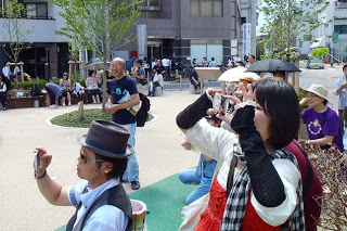 晴れた屋外でステージを見守る観客たちが楽しそうに写真や動画を撮っている様子の写真