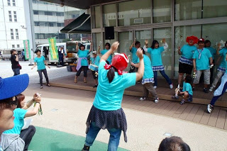 屋外ステージ前でオクトパス君の被り物を頭に被った人が、向かい合っているパフォーマーと元気に両手を上げて踊っている写真