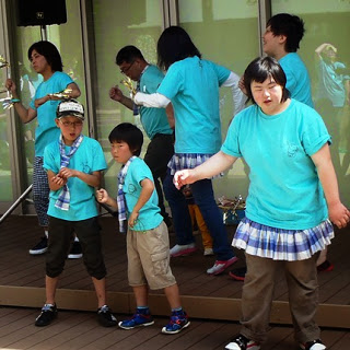 ステージ上で水色のTシャツを着た複数の人が真剣な表情で音楽に合わせて踊っている写真