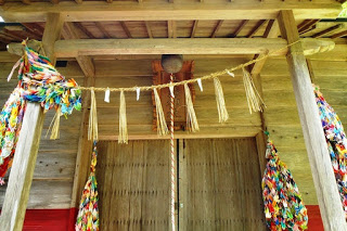 拝殿の入口にかけられた太い注連縄の下に、鈴と赤白の綱がぶら下がっており、両側にたくさんの千羽鶴が飾られている写真