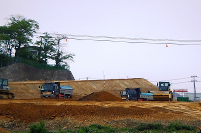 盛り土された広い土地の上でダンプカーやブルドーザーが作業している様子の写真