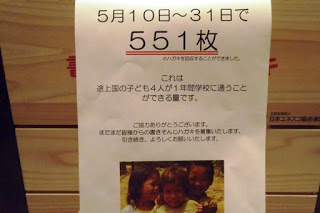 5月10日から31日までに551枚の寄付用はがきを集め、これによって途上国の子ども4人が1年間学校に通えることを伝える日本語の案内文と笑顔の子どもたちの写真が載った案内文を写した写真