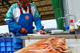 前掛け姿の作業員がまな板の上で鮭を包丁で丁寧にさばき、手前の板の上にさばいたオレンジ色の切り身が並んでいる様子の写真