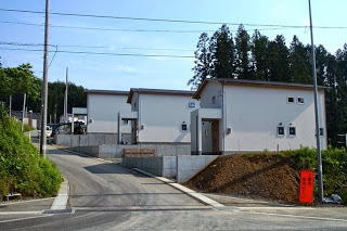 コンクリートの坂道の両側に新しく建てられた白い外壁の住宅が整然と並び、奥には林が見えている写真