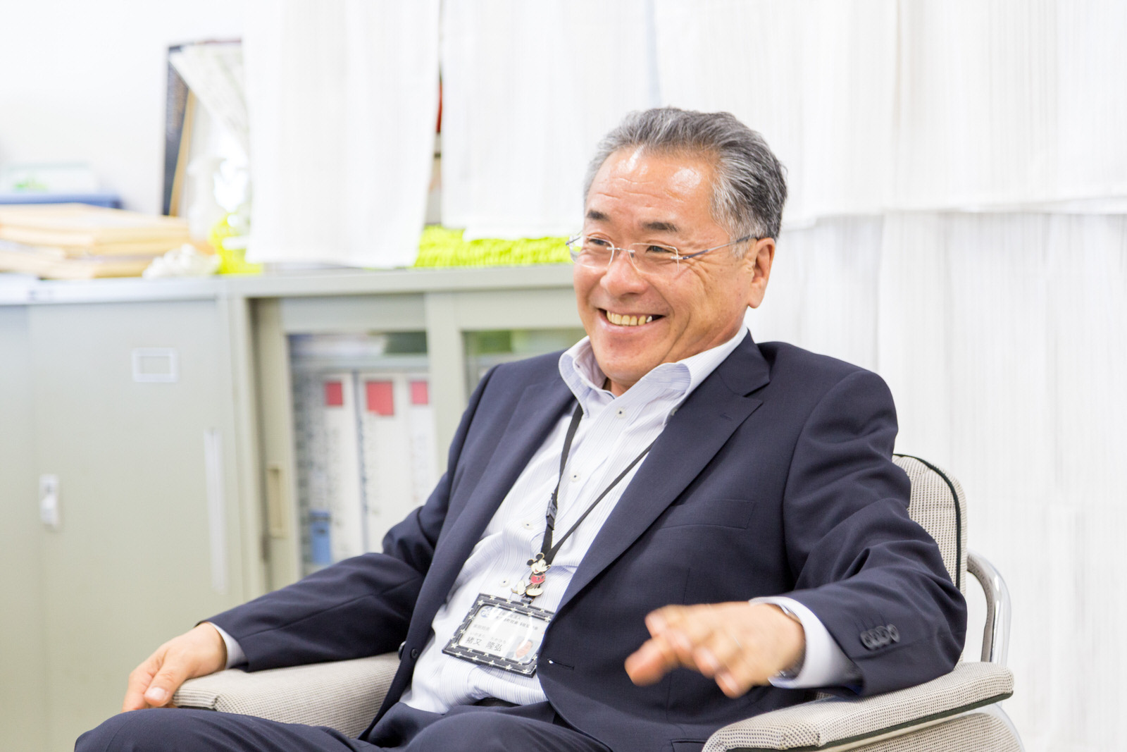 書類棚の前で椅子に座った猪又事務局長が満面の笑顔を見せている写真