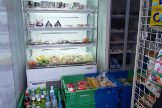 移動販売車の内部にある冷蔵棚におにぎりやサンドイッチ、サラダなどが並び、下の青と緑のかごには飲料やパンなどの商品が詰められている写真