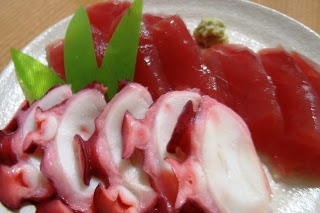 白い皿の上に赤身のマグロの刺身と、薄く切ったタコの刺身が美しく盛り付けられ、横にわさびが添えられている写真