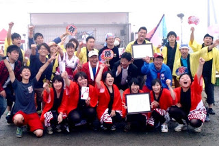 様々な衣装を着た人たちが笑顔で賞状を掲げ、歓喜のポーズを取って集合写真を撮っている写真