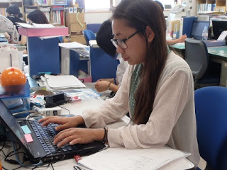 事務所のデスクでノートパソコンに向かい仕事をしている亀山さんを斜め横から写した写真