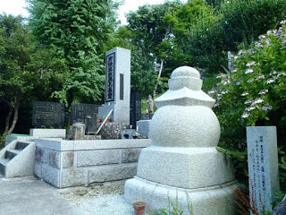 複数の石碑が立っている中に、白い石で作られた丸い供養塔が立っている写真