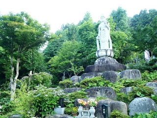 緑が豊かな境内の石段の上に白く輝く観音像が静かに立っている写真