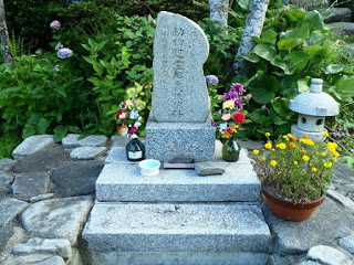 小さな石碑の横に花が供えられ、下にはプランターの花や小さな石燈篭が置かれている写真