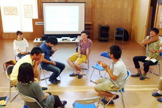 円形に設置された椅子に座った8人の参加者が、笑顔を交えながら意見交換している様子の写真