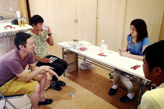 白いテーブルを囲んで、4人の参加者が飲み物を手にリラックスしながら話している写真