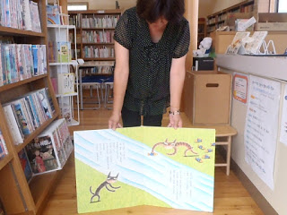 黒い服を着た女性が大きな絵本を開いて見せている写真