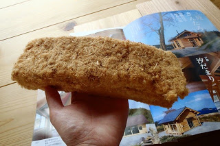 木造住宅のパンフレットの上で、手のひらに乗せた分厚くて茶色い断熱材の塊をアップで撮影した写真