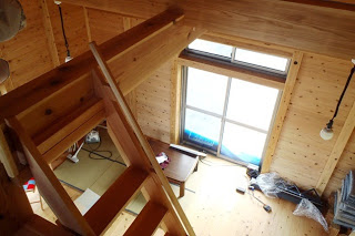 梁の上から見下ろした室内には、テーブルや畳スペース、積み重ねた座布団などがある写真