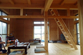 木の柱や梁がむき出しの室内に、座布団とテーブルが置かれ、梁へ続くはしごがある温もりのある空間の写真