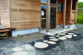 木の外壁の家の玄関前に、大小さまざまな丸い石が埋め込まれた飛び石の小道が続いている写真