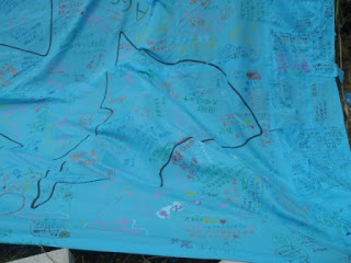 青い布に多くの手書きのメッセージやサインがカラフルに書かれている様子を写した写真