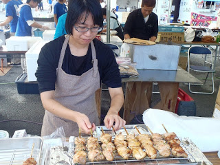 屋外の屋台でエプロン姿の女性が焼き鳥を焼いている写真