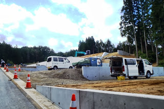 白い車や作業車がとまっている整地された宅地で、コンクリートの壁と重機が見える宅地の区画をつくっている途中の写真