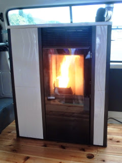 木の床の上に置かれた現代的な黒と白のペレットストーブの中で、縦長のガラス越しに明るい炎が勢いよく燃えている様子が写っている写真