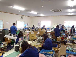 作業場の中で複数の作業員がミシンなどの機械を使って鞄製作などの仕事をしている様子の写真