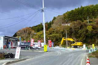 道路に徐行の看板が置かれ黄色いショベルカーが工事をしている道路工事中の写真