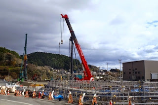 赤いクレーンが中心に写っていて、その周囲で橋や構造物の鉄骨工事が進められている建設中の現場の写真