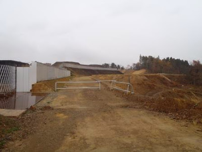 高台にある造成中の斜面に沿って工事車両用の未舗装道路が続き、奥には整備中の法面が見える造成地の坂道の写真