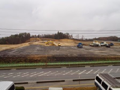 道路の向かい側に広がる整地された区画に重機やトラックが点在しており、建設準備が進められている整地地帯の写真