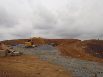 ショベルカーが盛土の上で作業しており、周囲には土と砕石が広がっている造成地の工事中の様子の写真