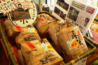 説明用のポスターが掲示され、紙袋入りの地元産米がカゴに並んで陳列されている写真