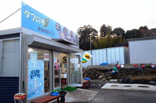 「タブの木」と書かれた青い看板が掲げられた直売施設の入口と外観写真