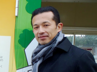 首にマフラーを巻いてカメラを見ている山本さんの写真