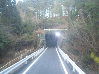 山道の中で両側にガードレールが設置され舗装された道路がトンネルにつづくいている写真。