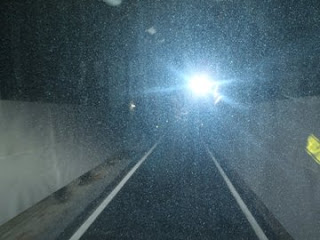 コンクリートの壁に囲まれた1車線のトンネル内で、奥に向かって続く舗装道路があり、暗い中で天井の照明が道を照らしている写真