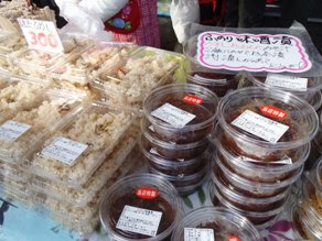 透明のパックに入った炊き込みご飯など色々な商品が机の上に重ねて陳列されている様子を写した写真