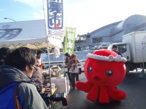 赤いタコのキャラクターオクトパス君がテント横の通路を歩いている様子を写した写真