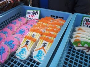 正月用の宝船や松・日の出などの模様が描かれた細工かまぼこが3種類が青いかごに並べられている写真