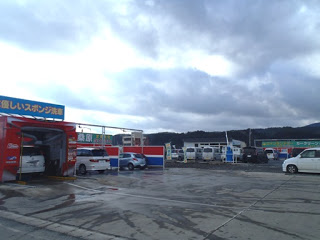 仕切られた複数の洗車スペースに車が停まり、洗車作業が行われていて、順番待ちの車も停車している様子を写した写真