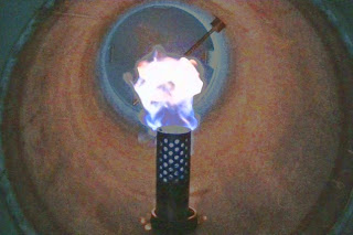 円筒形の装置内部で青白い炎が燃えており、バイオガスなどの燃焼試験を行っている様子の写真