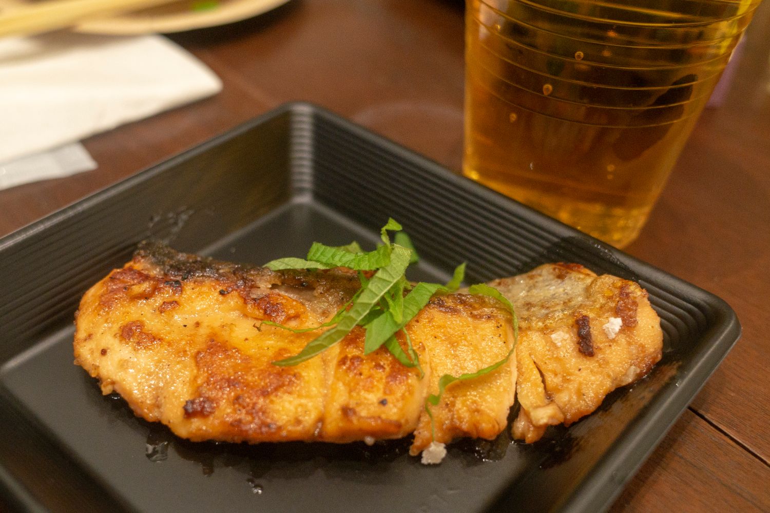 黒い四角の皿に刻んだ大葉がのっている秋鮭のムニエルが盛られた写真