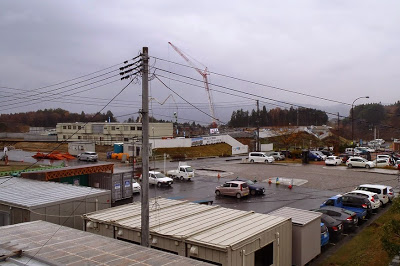 全体に曇り空が広がる造成地内に整備中の重機や車両が点在し、奥に見える工事用クレーンが作業を行っている整備地の写真