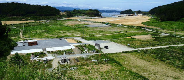 手前に石仏や石灯籠があり奥に広がる草地と遠くに海が見え造成された土地が広がっている慈眼寺墓地から写したパノラマ写真