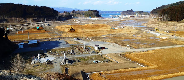 手前に石仏や石灯籠があり奥に広がる草地と遠くに海が見え工事が進んでいる整備された土地が広がっている慈眼寺墓地から写したパノラマ写真