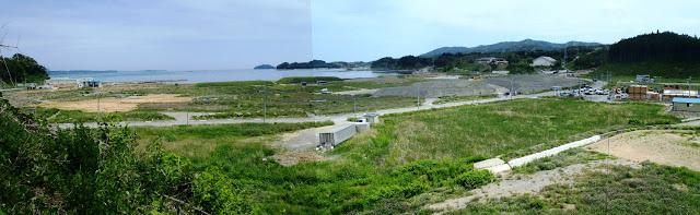 遠くに海が広がり、道路が走り緑が茂る大きな更地が広がるパノラマ写真
