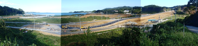 海沿いの広い造成地に重機が点在し、新たな道路や区画整備が進められている中、まだ更地の部分が多く見られるパノラマ写真